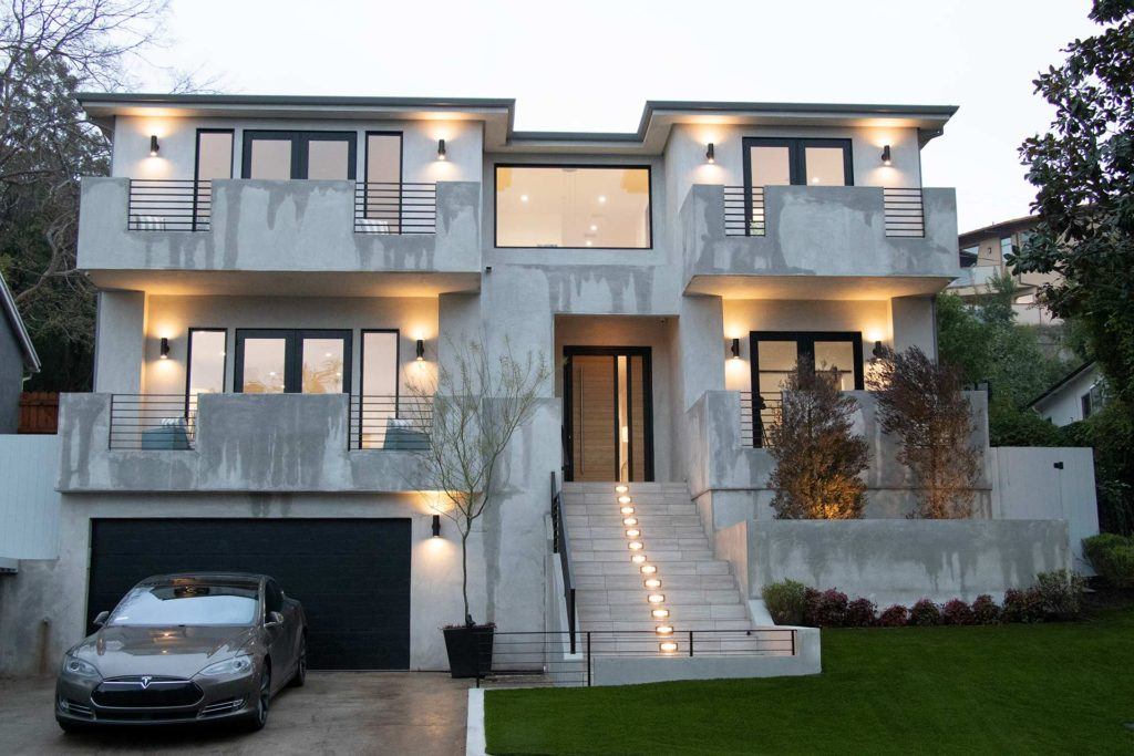 exterior of grey home at dusk with exterior lights and car parked in driveway