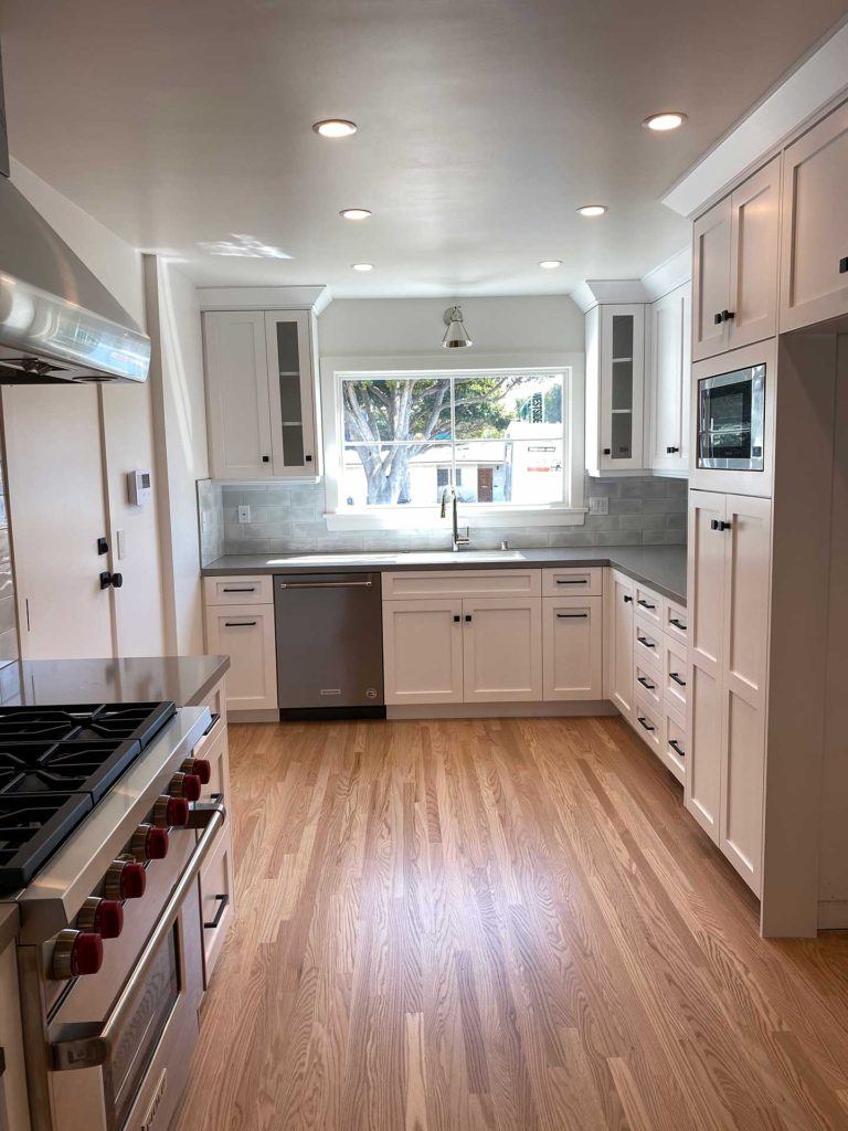 renovated kitchen with stove washing machine and white cabinetry