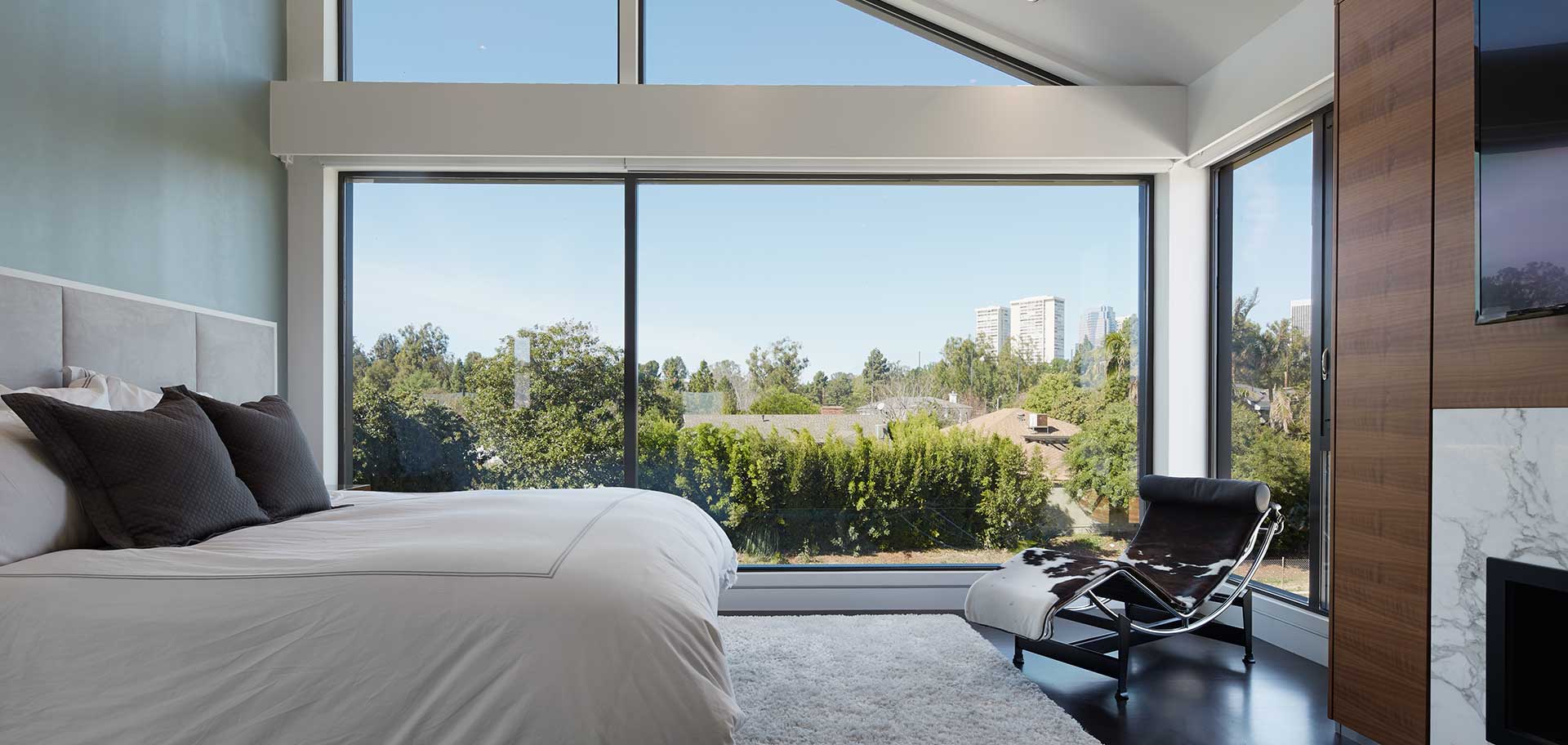 bedroom with bed chair fireplace and mounted tv with large angled window