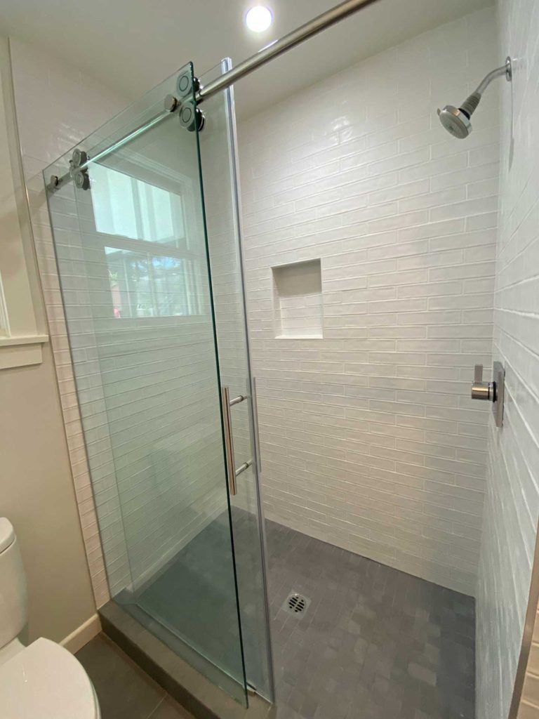 shower with open glass door and white tiles