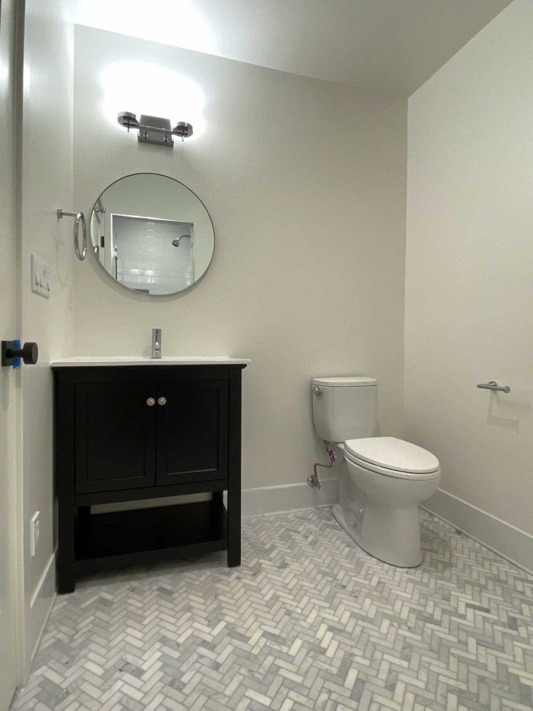 bathroom with toilet and black vanity with circular mirror